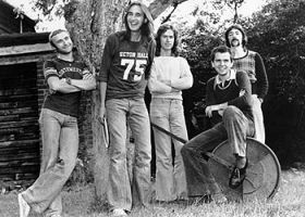 o Genesis em 1974, da esquerda para a direita: Phil Collins, Michael Rutherford, Anthony Banks, Peter Gabriel (sentado) e Steve Hackett